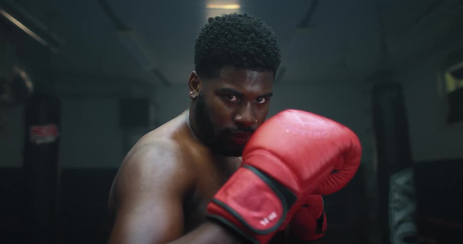 A male boxer poses in a gym with his red gloves near his face
