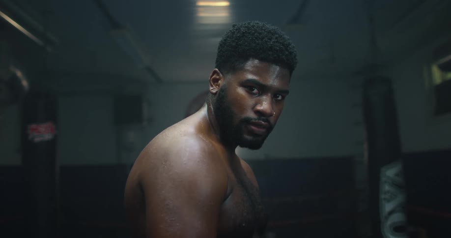 Shirtless strong muscular man looking at the camera inside a dimly lit gym