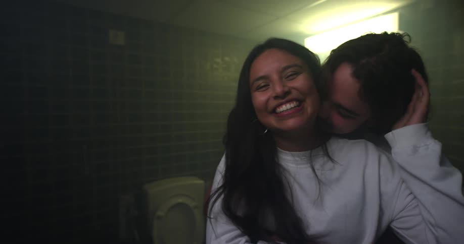 A teenage girl smiles and laughs as her boyfriend kisses her on the side of her neck