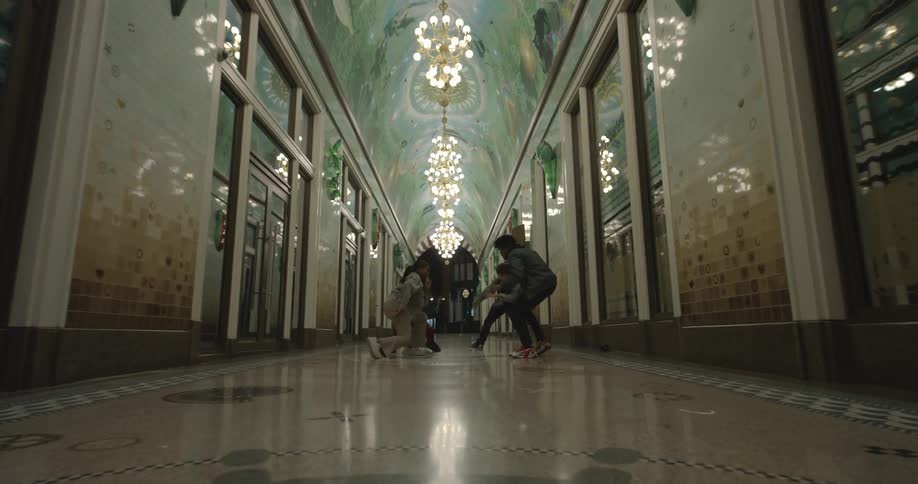 A group of four people dance hip hop in the hallway of an ornate office building with marble floors and walls