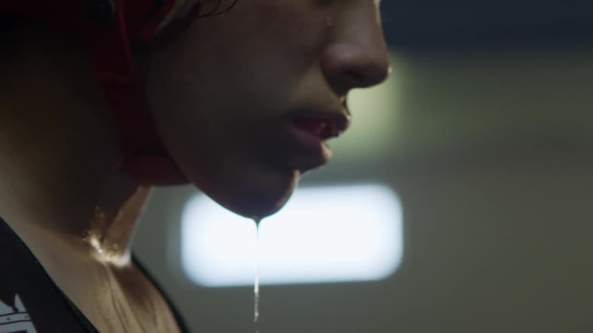 A stream of heavy sweat drips from a womans chin as she stands in front of a white screen