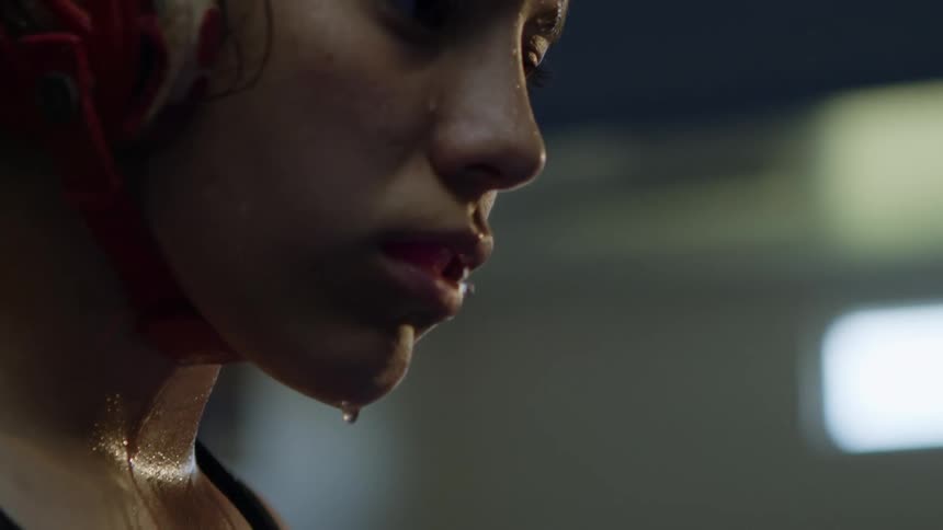 Beads of sweat drip from a womans chin as she stands in a dark studio