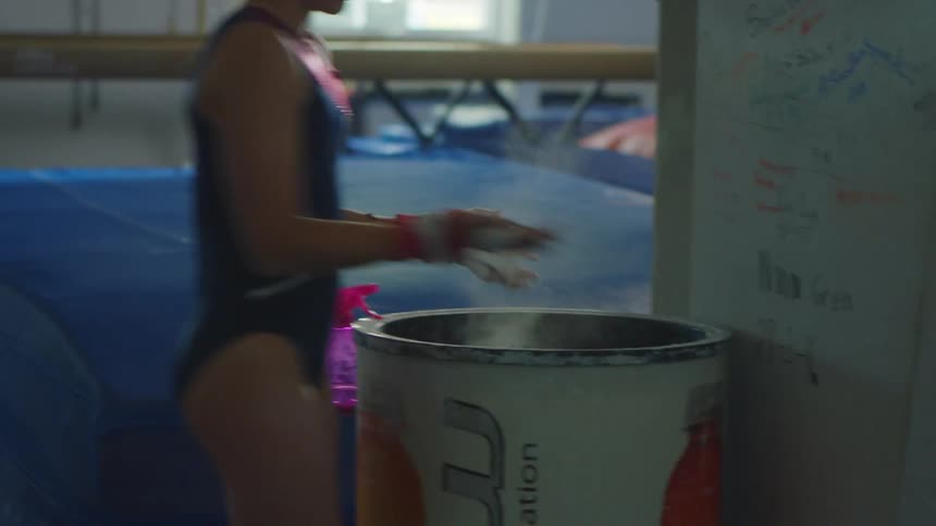 Teenage gymnast dusting her hands getting ready to practice inside of a gymnasium