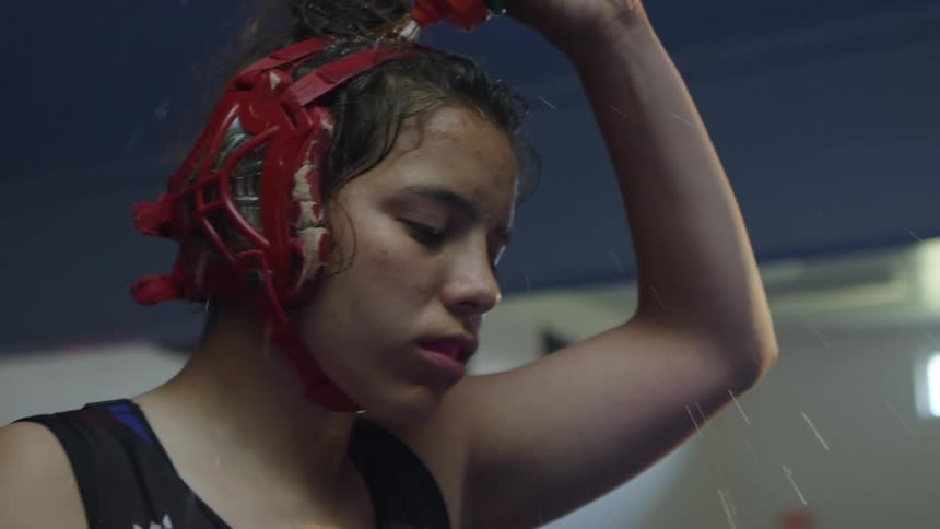 Woman in boxing gear pours water onto her head out of a water bottle