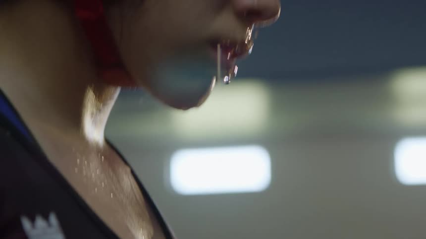 A woman with headgear and a mouthguard standing in a gym pouring water on her head