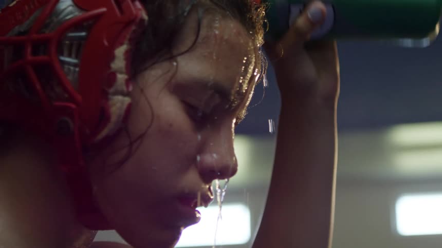 Sweating young woman in wrestling gear pours water over her head