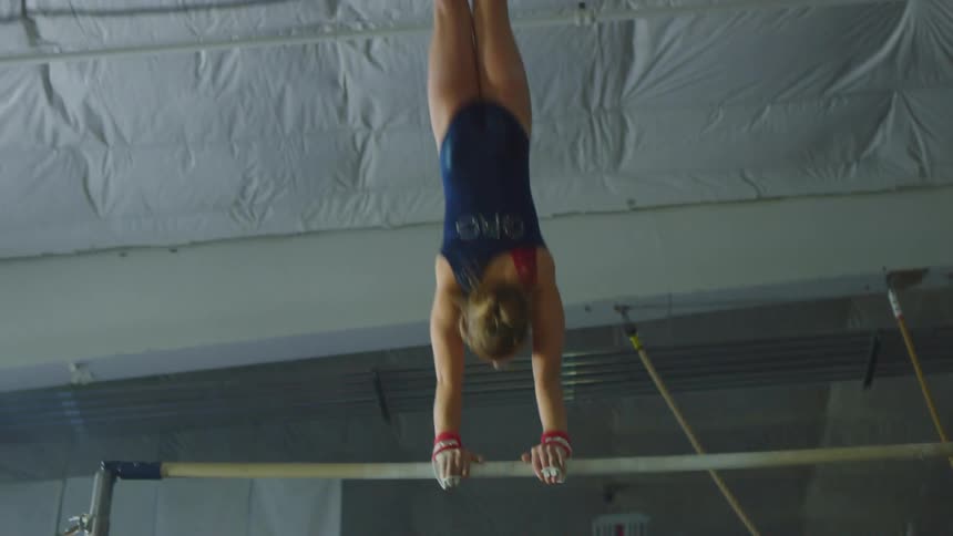 A young girl doing gymnastics swings around a bar a flips off
