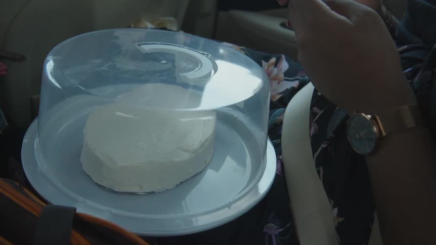 A woman sitting in a car holding a cake inside a container on her lap