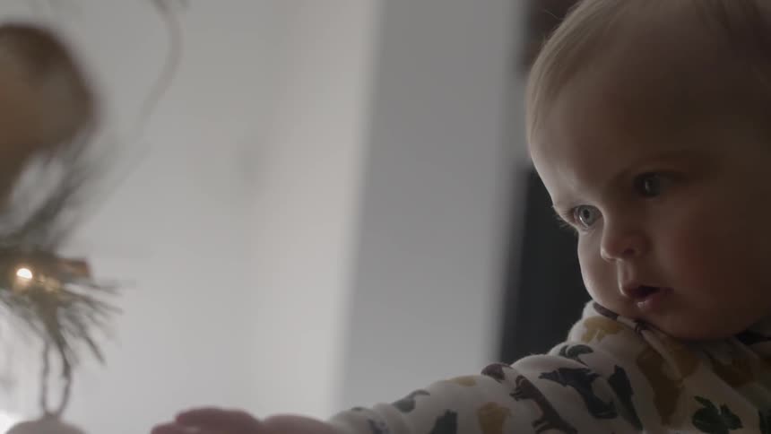 An infant reaches out and touches an ornament on a christmas tree