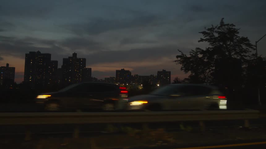 View of a city with tall buildings from a moving car traveling on a highway next to other vehicles