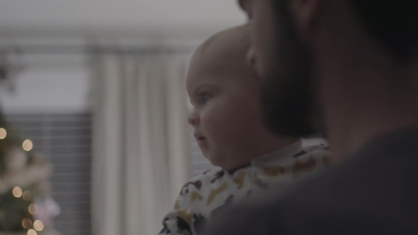 Bearded man holding an infant with their christmas tree in the background