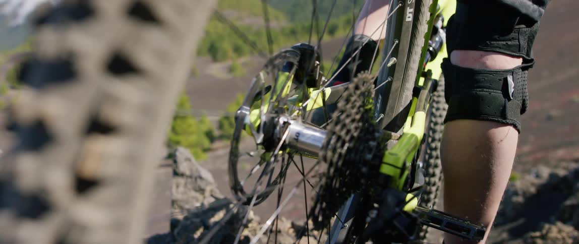 A male on a bike in the mountains with a close up of the bike wheel