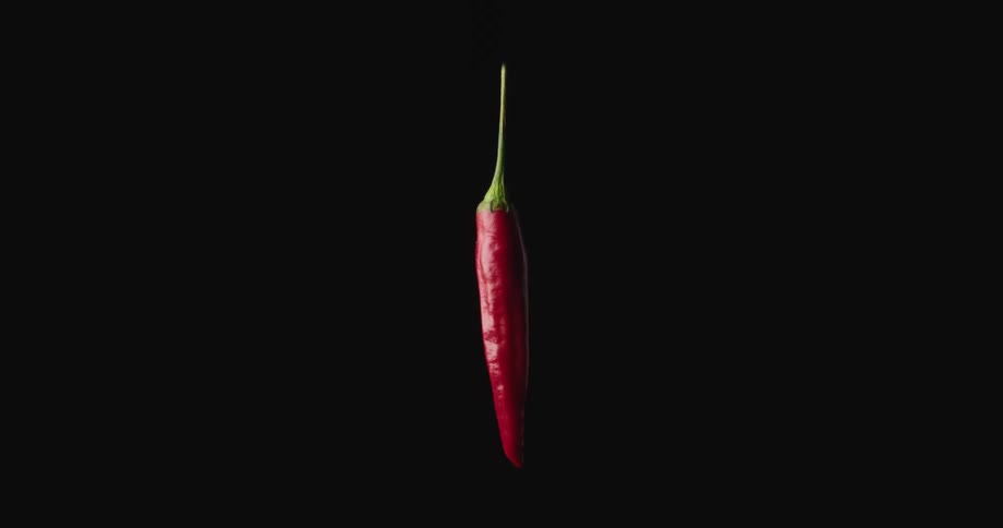 A red chili pepper spins while hovering in the air in a dark space