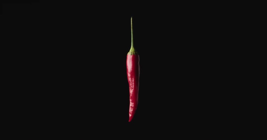 Floating red hot chili pepper spinning against a black background