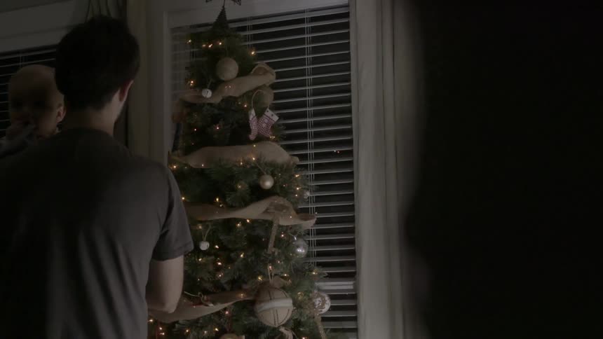 A man looks at a christmas tree while holding a baby