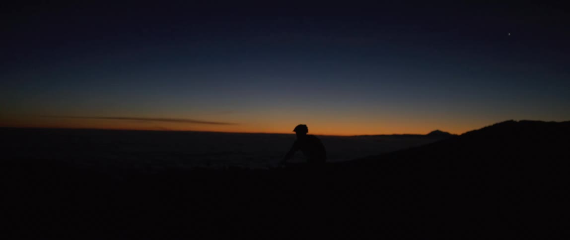 A cyclist rides a bicycle through uneven terrain at sunset