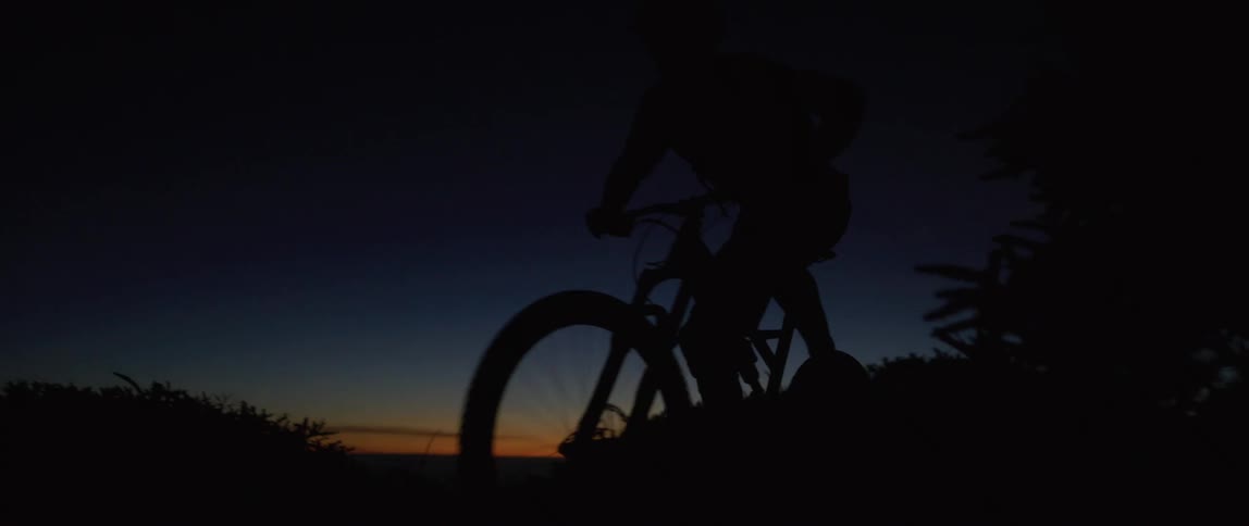 A silhouetted bicyclist pedaling outside at dusk