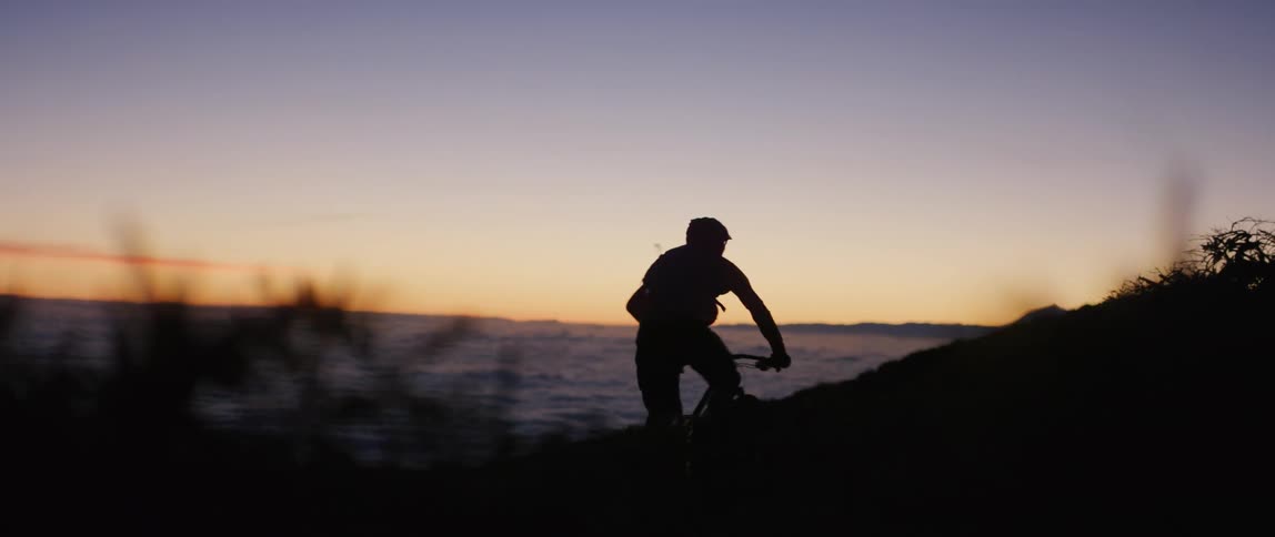 A male bike riding up a hill at dawn