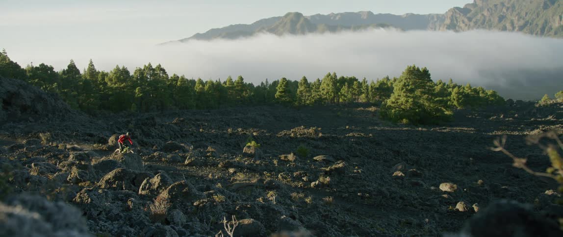Cyclist driving a bicycle on a trail at the top of a mountain range over the clouds