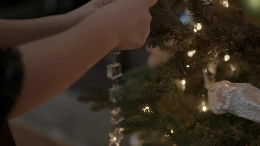 Close up of hands placing ornaments on a christmas tree