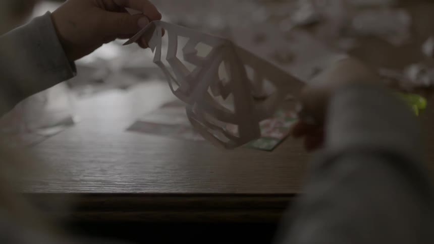 A child holds up and starts to unfold a paper cut out snowflake