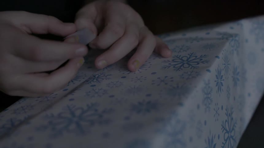 A child's hands are seen as they apply a piece of tape to wrap a gift