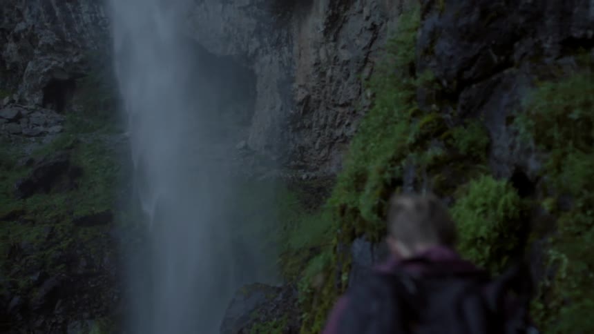 People hiking on rocky terrain toward a waterfall
