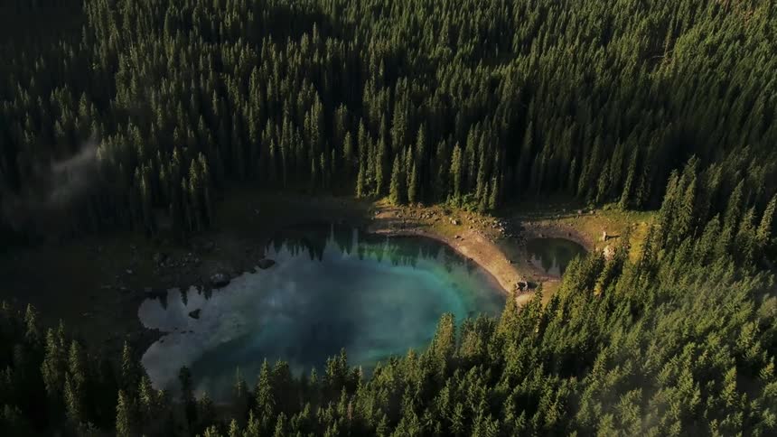 Lake in a forests area with two clouds of smoke in the background and a road with a car driving on it at the bottom of the frame