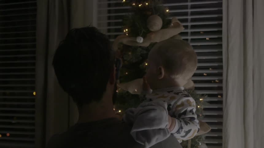 A man holding a baby in his arms as he approaches a christmas tree