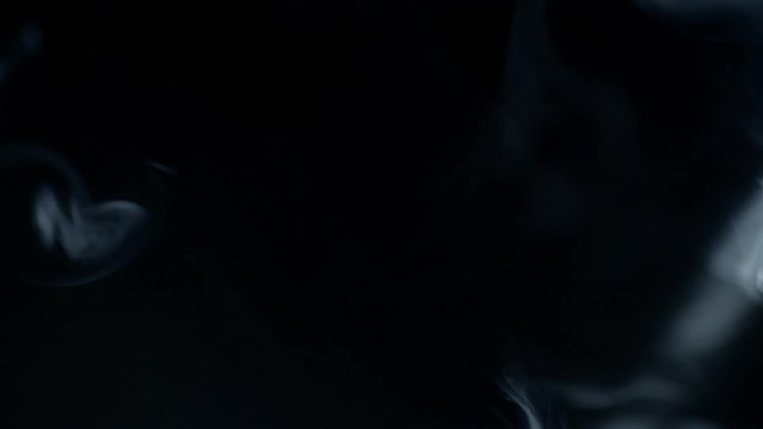 Smoke slowly drifts through a darkened space and is briefly illuminated by a beam of light