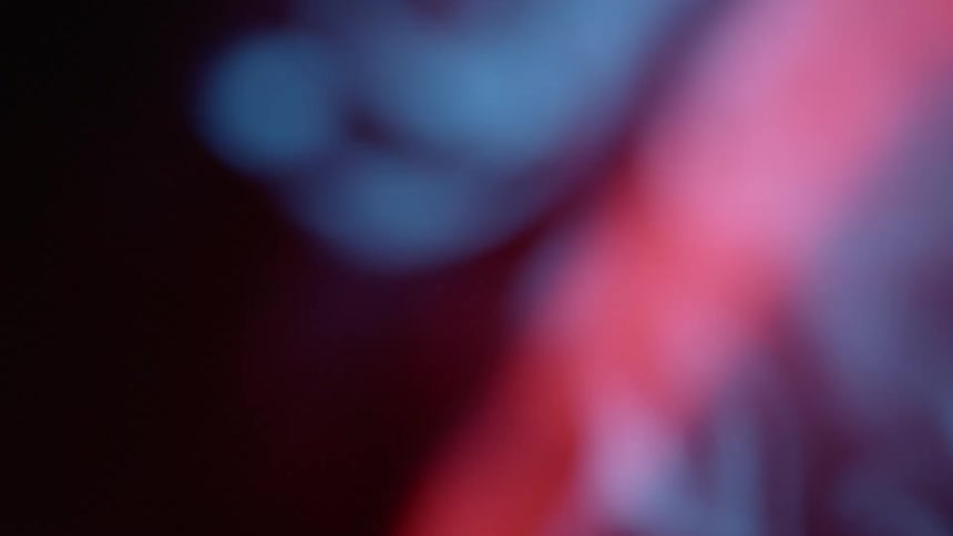 Smoke rises and drifts in front of a red beam which causes the smoke to take a pink hue