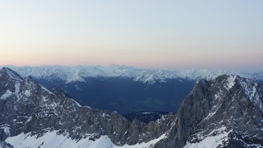 An aerial view of mountains topped with snow with a hazy sky