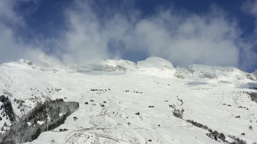 A snowy mountainside near large fluffy clouds and a blue sky