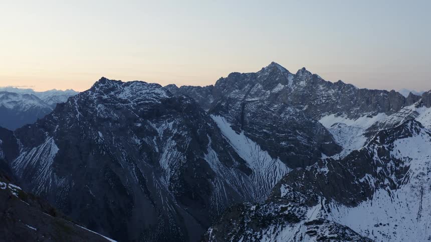 Aerial view of the snow covered peaks on a mountain range at sunset