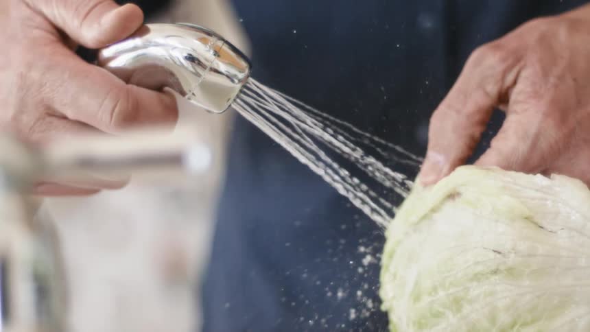 Man washing a head of lettuce with a faucet hose