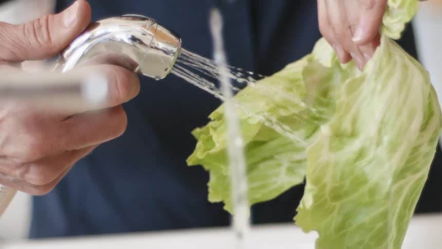 Man washing a leaf of lettuce with water on the sink