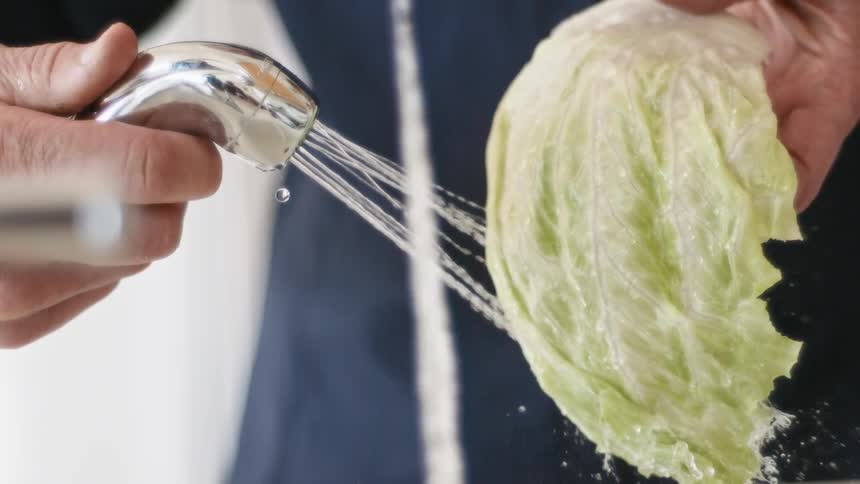 A person with a faucet washing lettuce with water