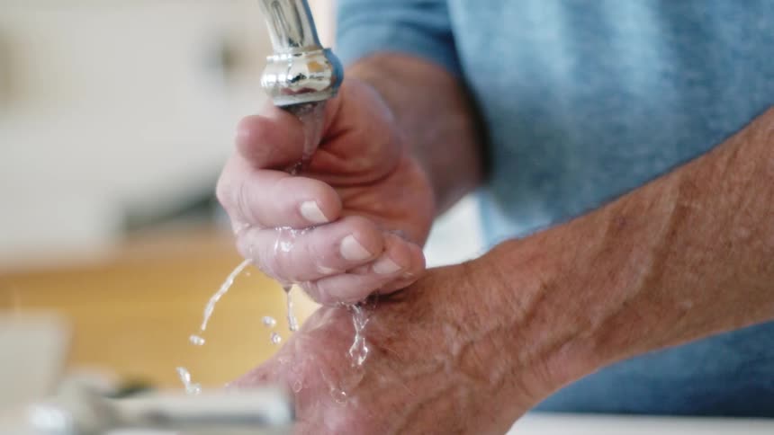 A man washing his hands under a metal faucet