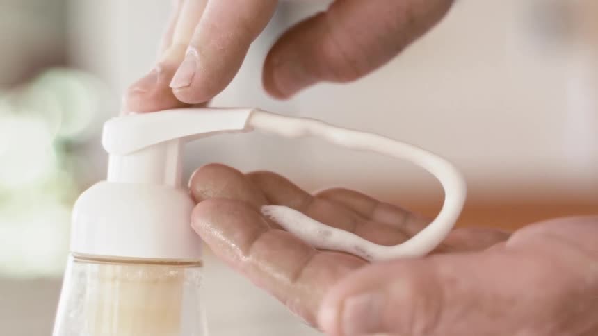 Hand pressing down hand dispenser over the sink on a bathroom