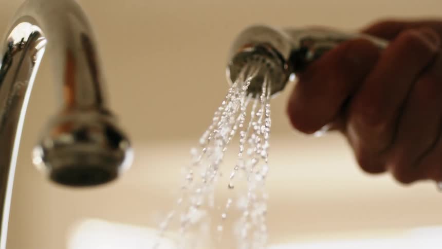 A person holding a faucet over a sink as water falls