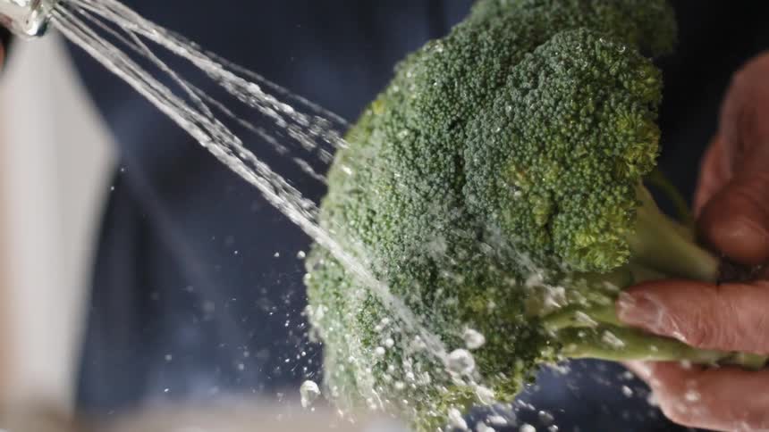 Man uses a sprayer to rinse off a head of broccoli