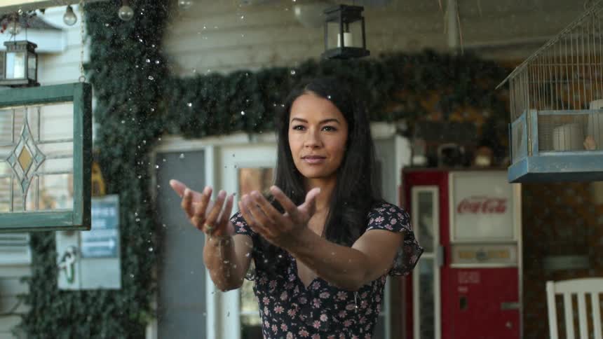 A woman holds her arms out in front of her with her palms up as drops of water fall on and around her hands and arms