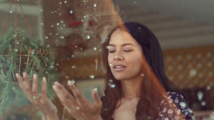 A woman stands outside in a short sleeve dress with her hands up as snow falls