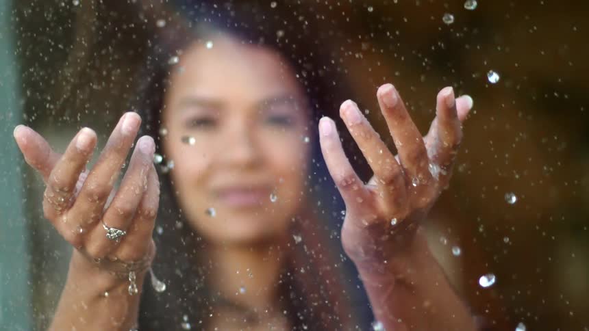 A woman reaches out her hands to touch falling rain or water in sunlight