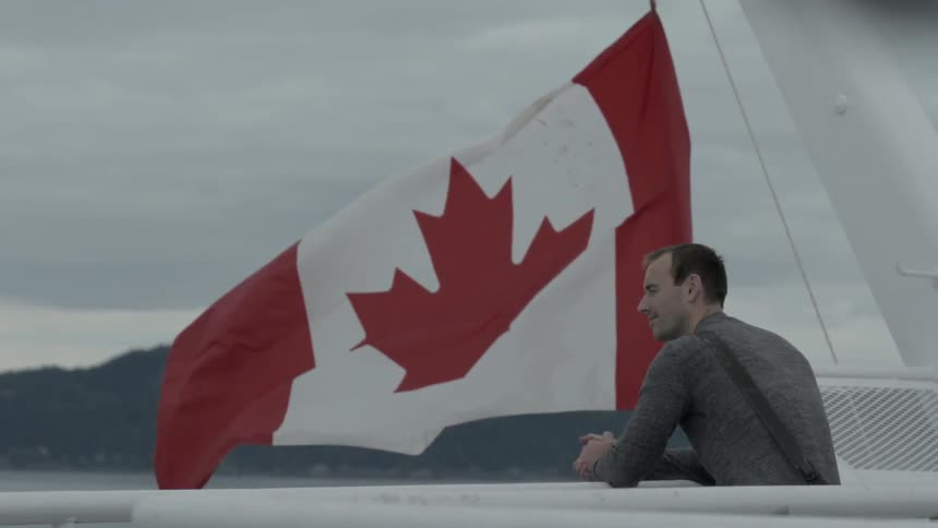 Man leaning on a railing with a large canadian flag waving next to him