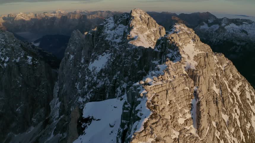 Mountain with some snow sunlight on one side shadow on the other at sunset with other mountain ranges against the horizon in the distance