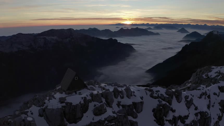 A small triangle shaped home sits on top of a snow covered mountain