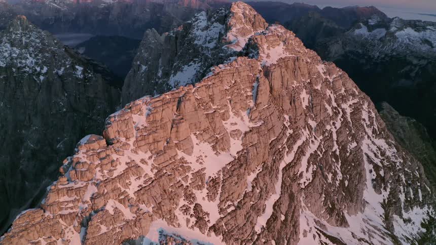 An aerial view of a mountain range with snow visible and a pink sky