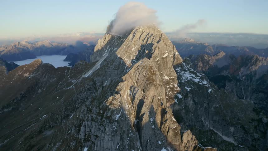 The summit of a towering rocky mountain is obscured by a gray cloud
