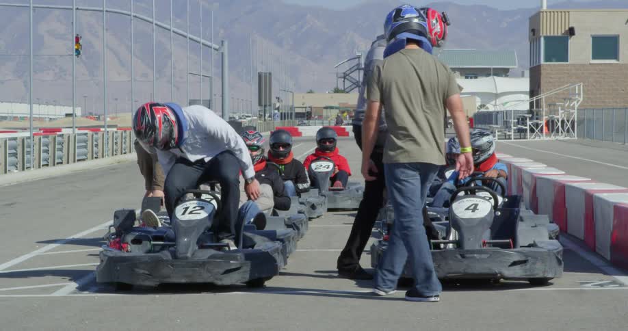 Men climbing into and securing go karts on a speedway during the day